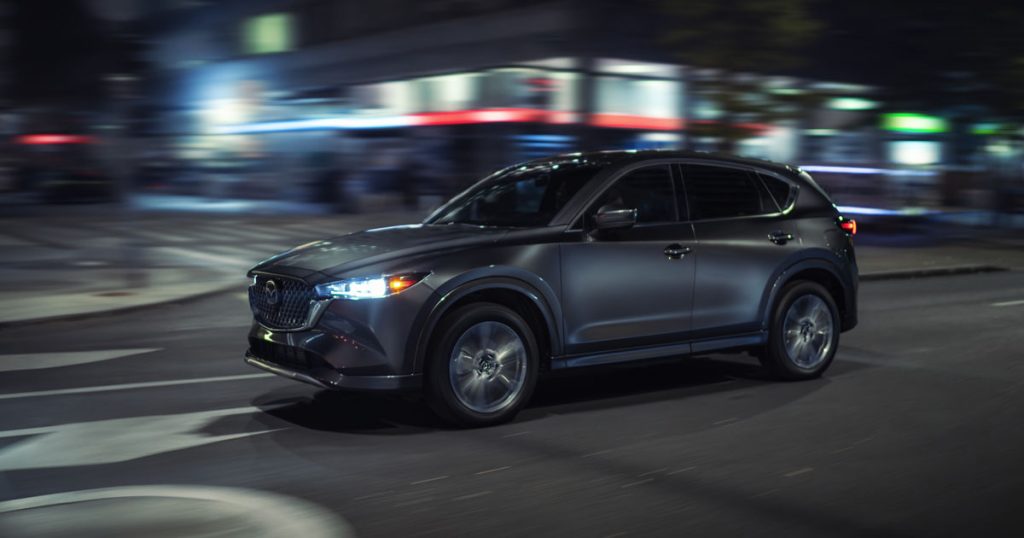 A 2025 Mazda CX-5 driving fast through city streets at night.