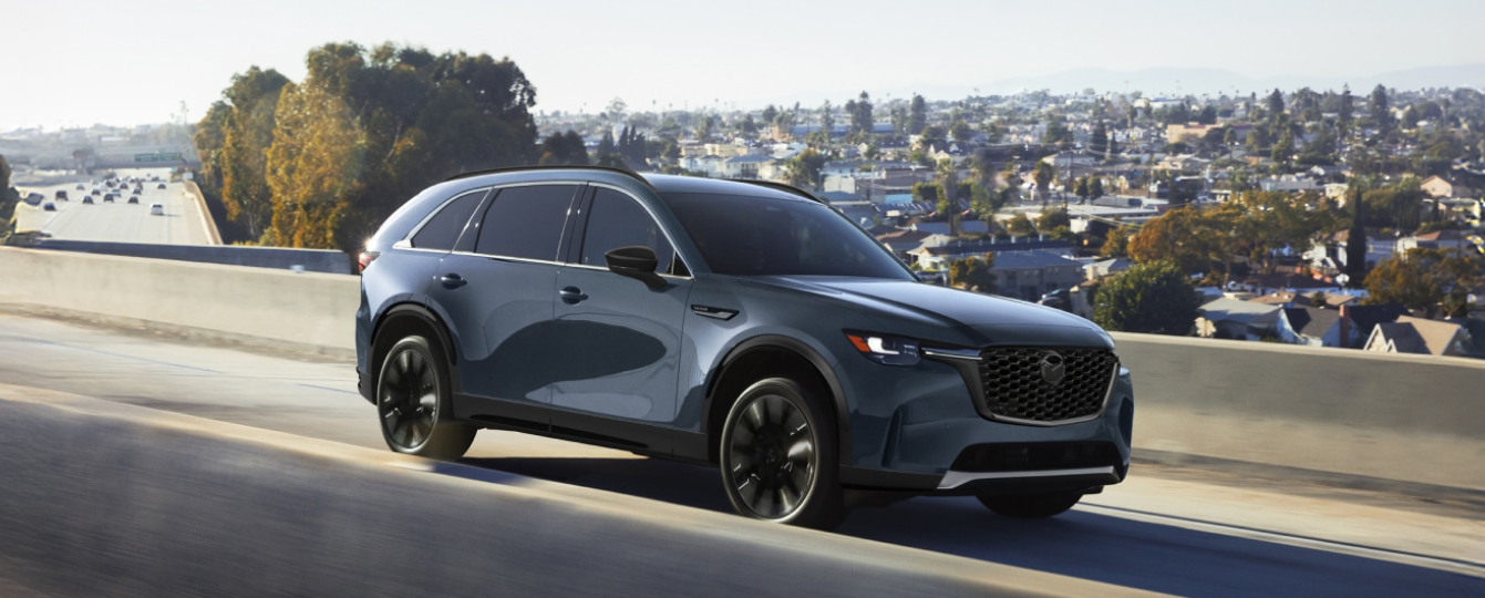 The 2026 Mazda CX-90 drives on a sunny road.