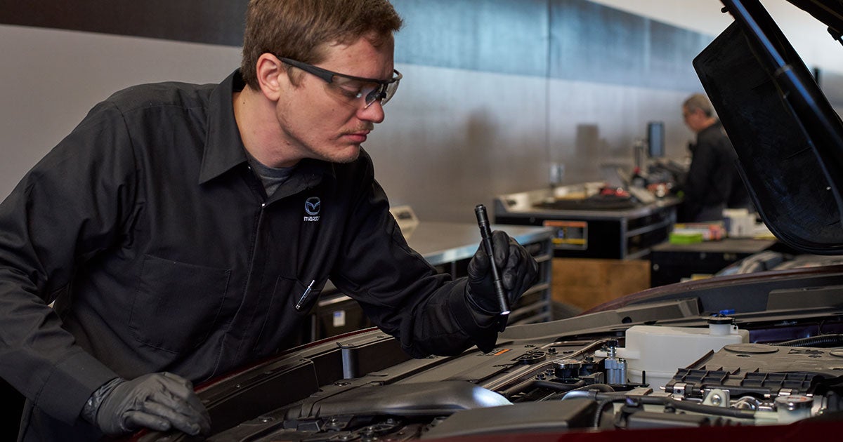 A service technician inspecting a vehicle's engine with a flashlight